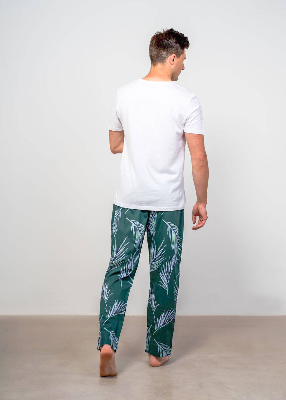 Back shot of model wearing cabo de rama mens pyjama bottoms dark green leaf print